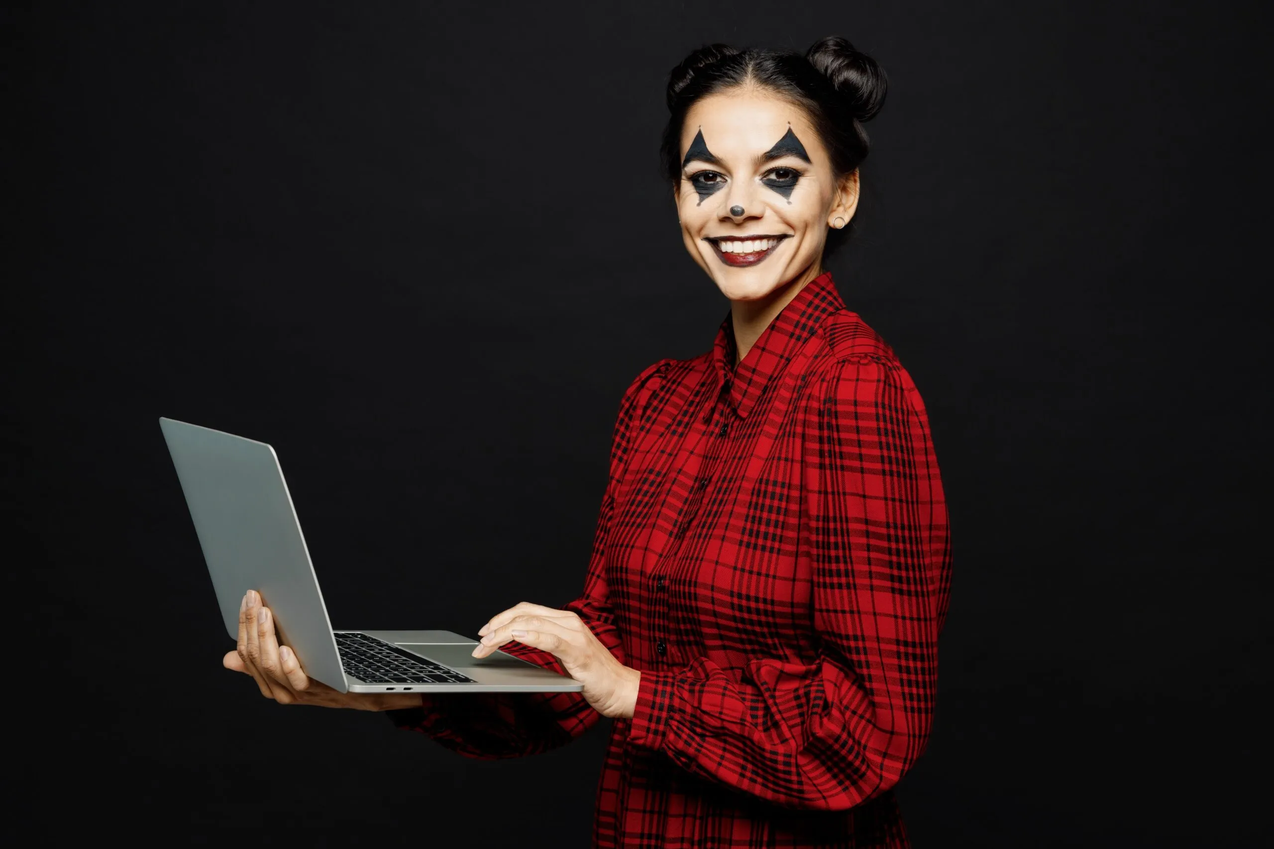 Woman in red checked tip with painted face holding laptop for Halloween cybersecurity webinar