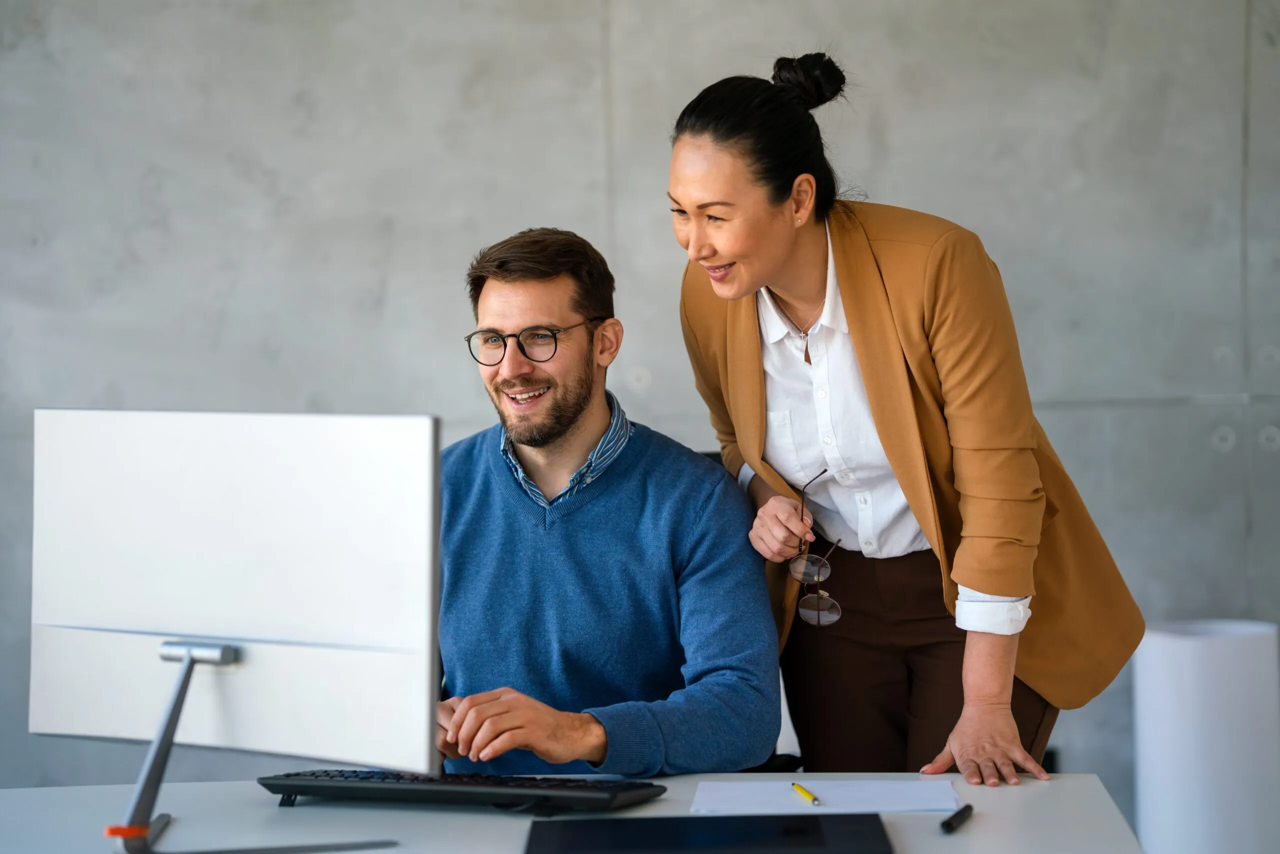 Man with glasses and blue jumper and middle aged women in beige jacket discuss Essex IT consultancy while looking at desktop.