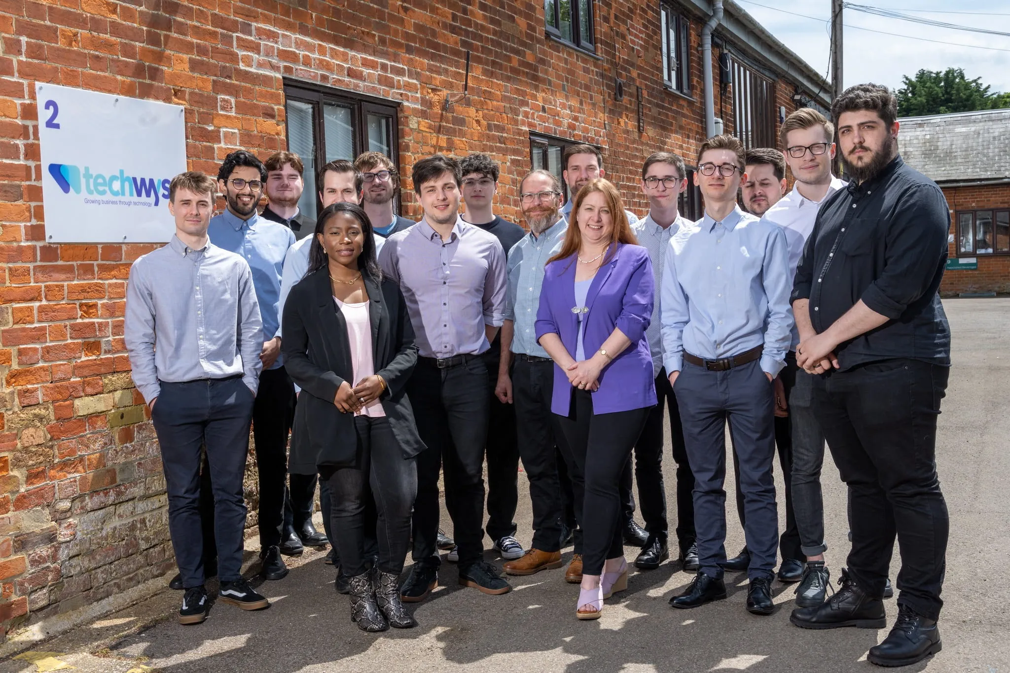 Managed IT services in Essex provided by TechWyse, showing full team in matching TechWyse hoodies smiling in front of brick wall