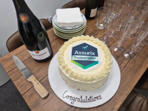 A table with a bottle of Champagne, a cake with the Assurix logo, plates with napkins and Champagne glasses on it